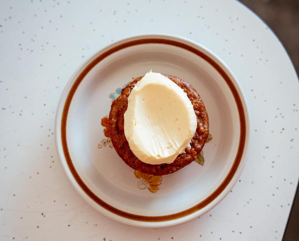 A muffin with cream cheese on a white plate with orange border on a table.