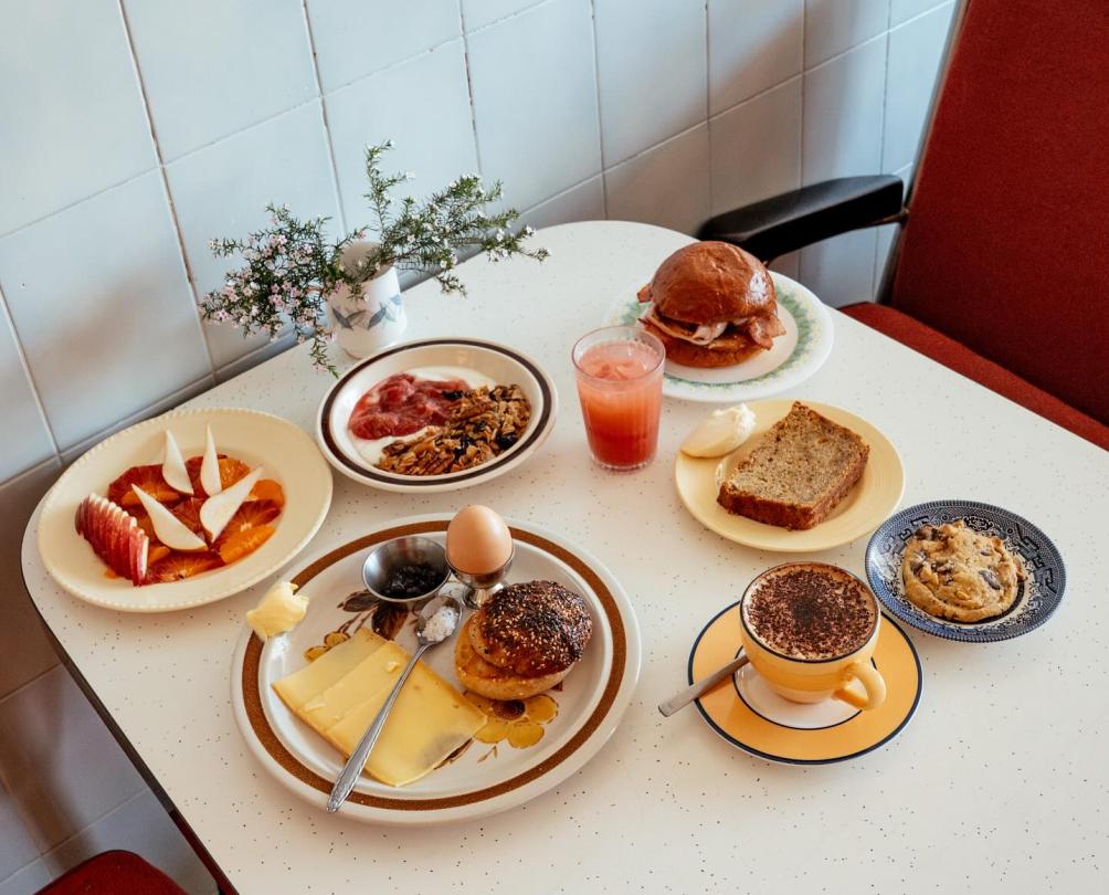 A selection of breakfast dishes on a white table with soft red chairs either side.