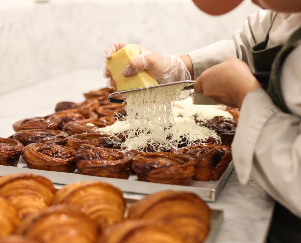 A pastry chef grates cheese over a tray of pastries.