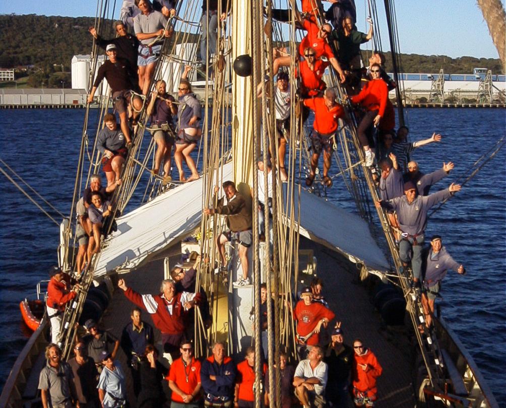 A large group of people aboard a tall ship, all waving at the camera.