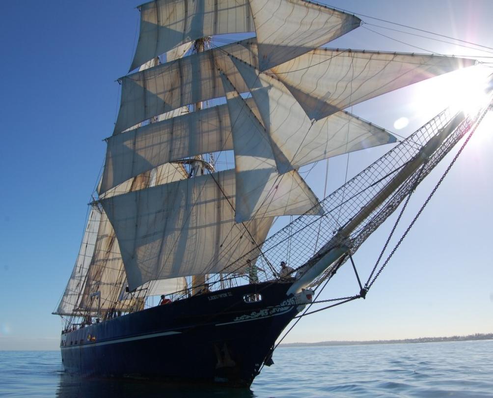 A tall ship with several masts sails on the ocean under a blue sky.