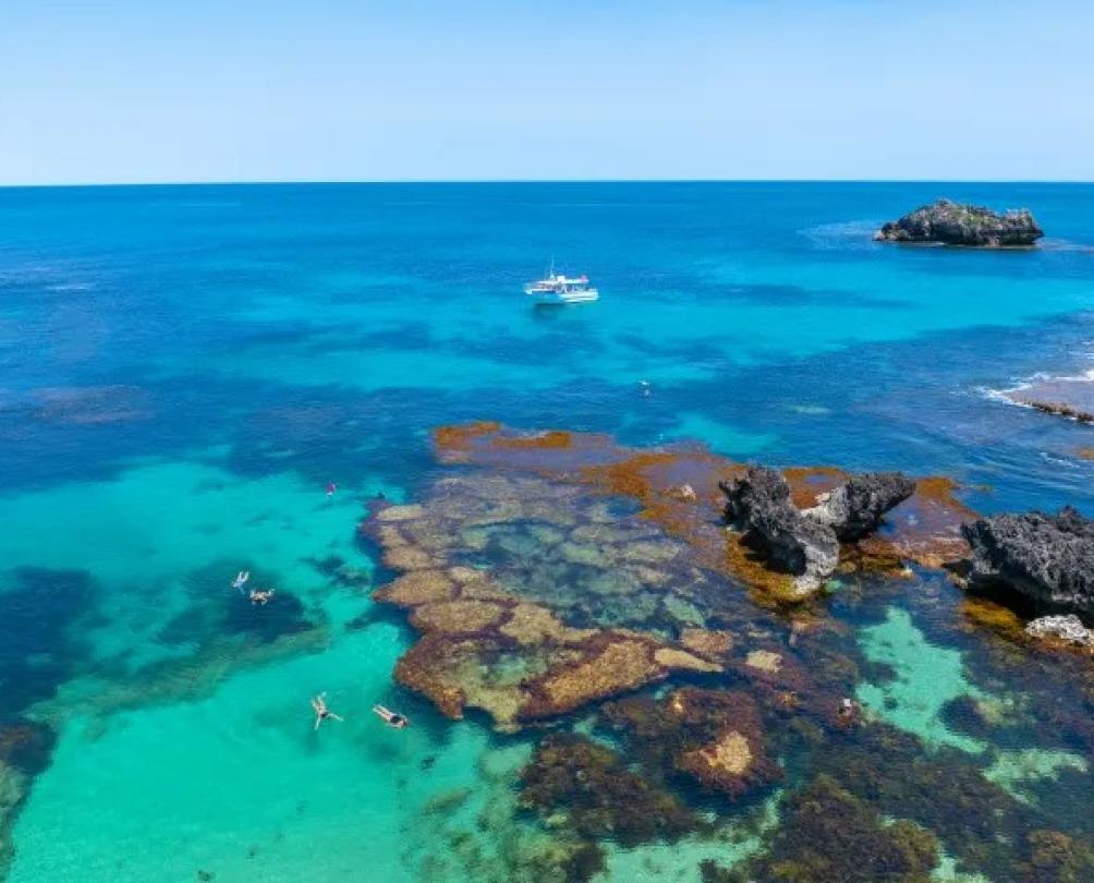 a beautiful blue/green ocean with some rocks and a boat in the background 