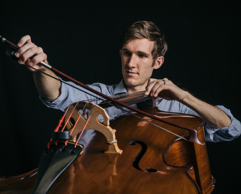 a man playing a cello in a blue shirt with a black backgroun
