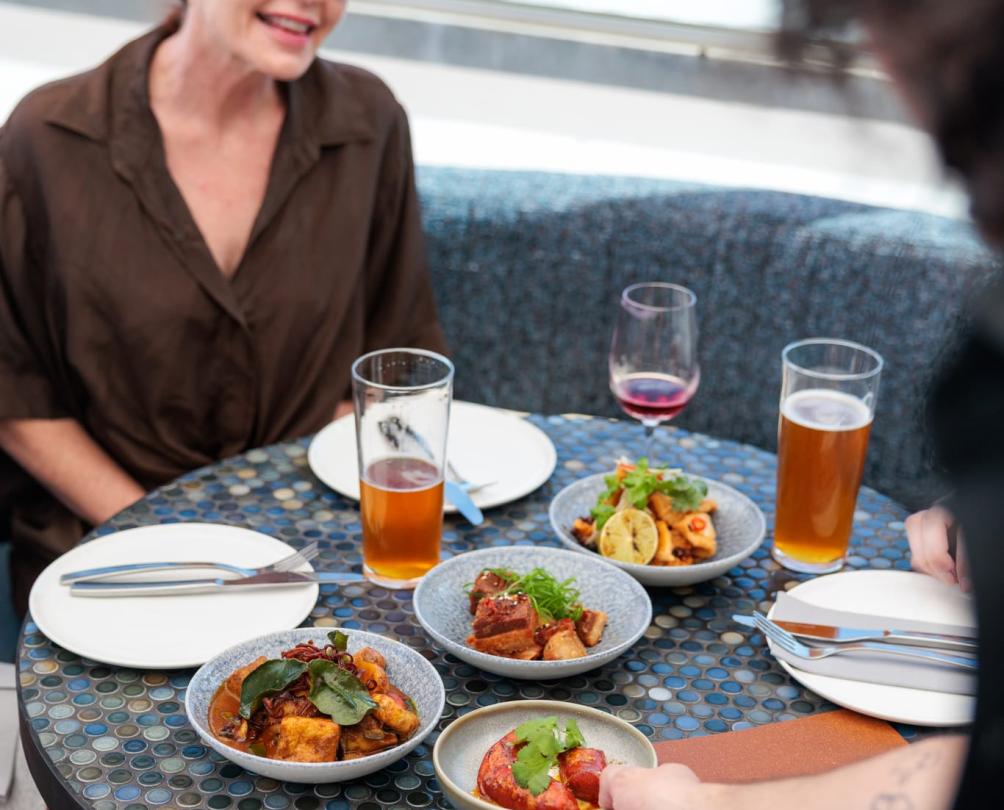 a woman sitting in front of a table of food while the hand of a server reaches down to place the food