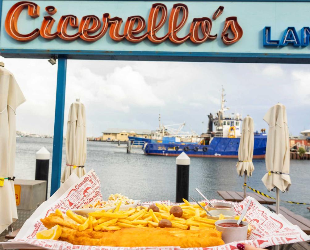 someone holding a plate of fish and chips with the Cicerello's sign in the back