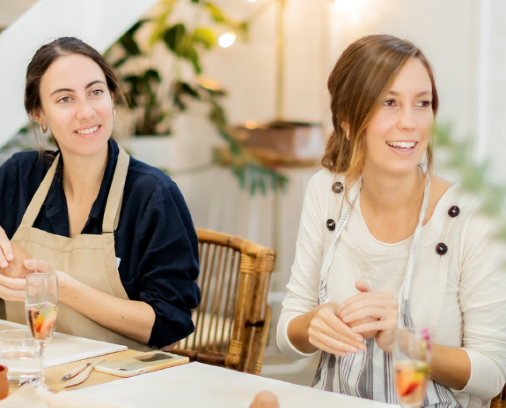 two women smiling and working on crafts at a table