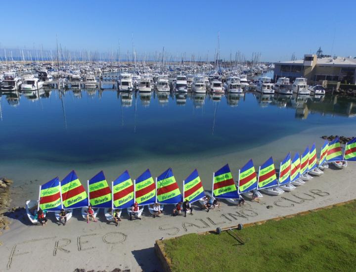  Sailing boats lined up on the shore with striped sails and the words FREO SAILING CLUB written in the sand