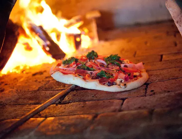 photo of a pizza going into a woodfire oven. 