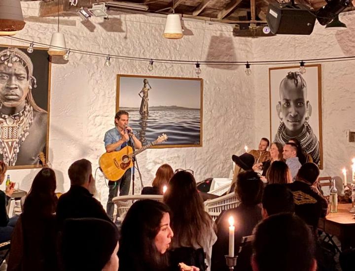 a musician plays guitar to an audience in an intimate candlelit gallery with large scale portraits on white walls