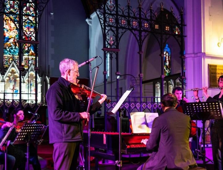 orchestra performs in front of stained glass windows in a church
