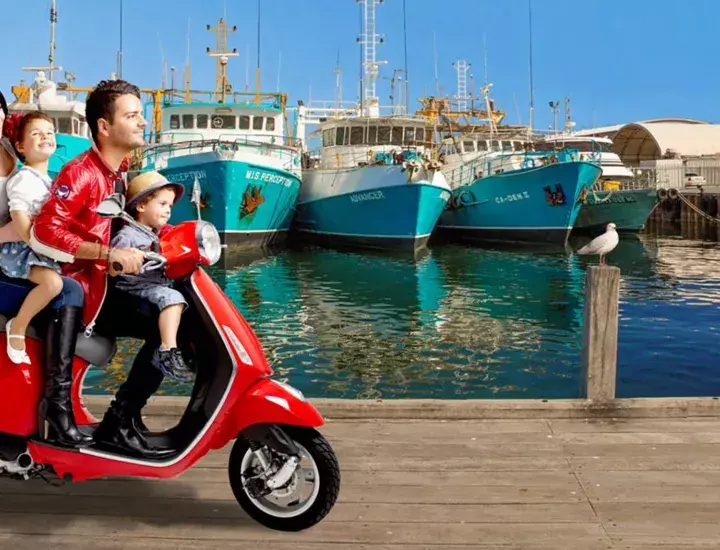 A family riding a red scooter through Fishing Boat harbour