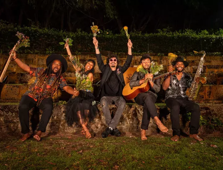 Five people holding flowers and instruments sitting on a wall.