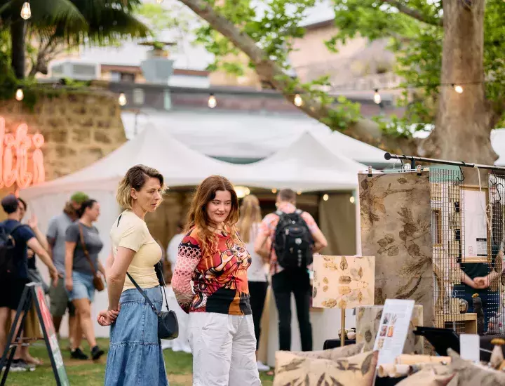 Two women admire a stall with handmade goods.