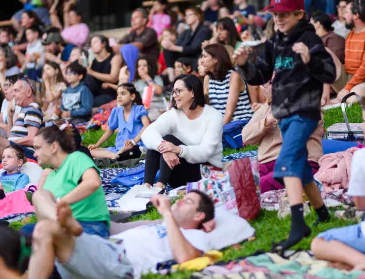 A group of people on a sloped lawn watching a movie
