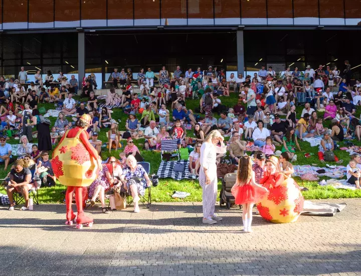 Two people dressed as Christmas baubles entertaining people on a sloped lawn.