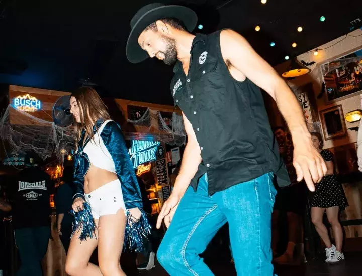 A man and a woman line dancing in a western bar.