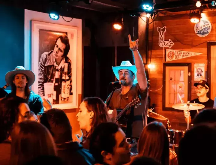 A man in a cowboy hat plays guitar in front of a dancing crowd.