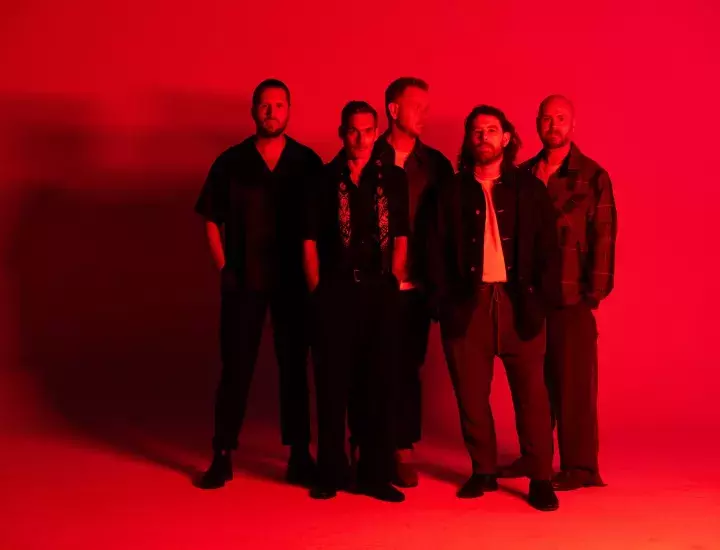 Five men stand in a room illuminated in red light.