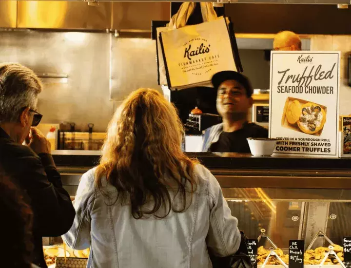 A couple standing at a food counter ordering food, a sign for Truffle Chowder on display