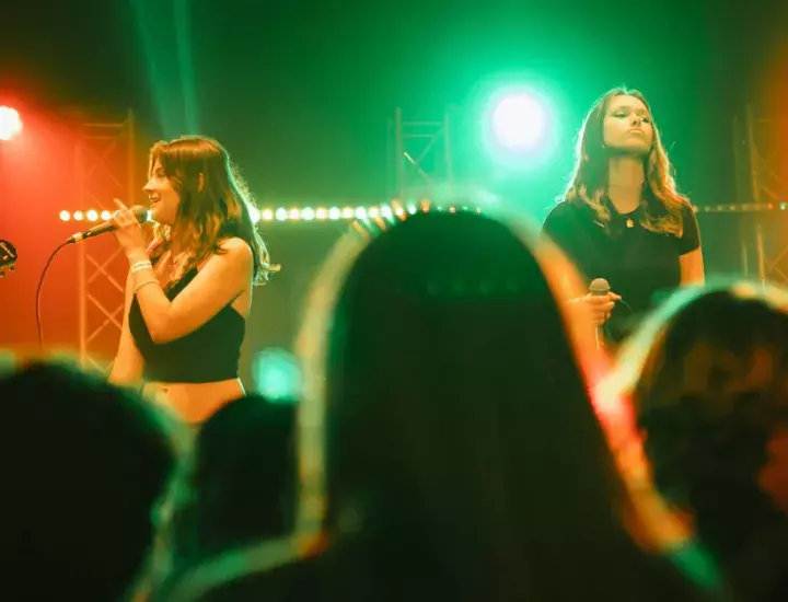 a few females singing in front of a crowd in a room that is lit up