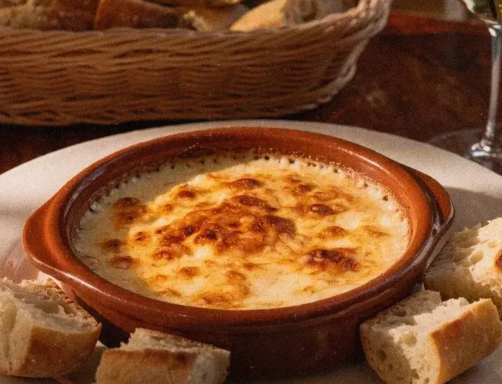 an image of the top of a fondue dish with some cut bread around it and a glass of wine in the background